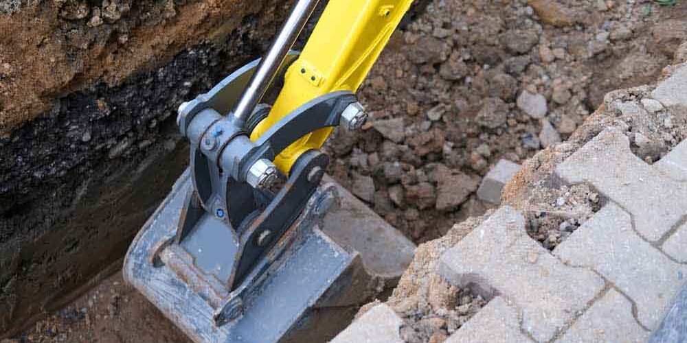 excavator bucket digs earth in trench on street, concept of repairing urban communications, conducting electrical networks to buildings, underground laying optical fiber for communication